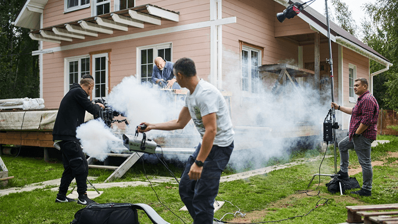 Мужчина с помощью дым-машины делает дым на съемочной площадке